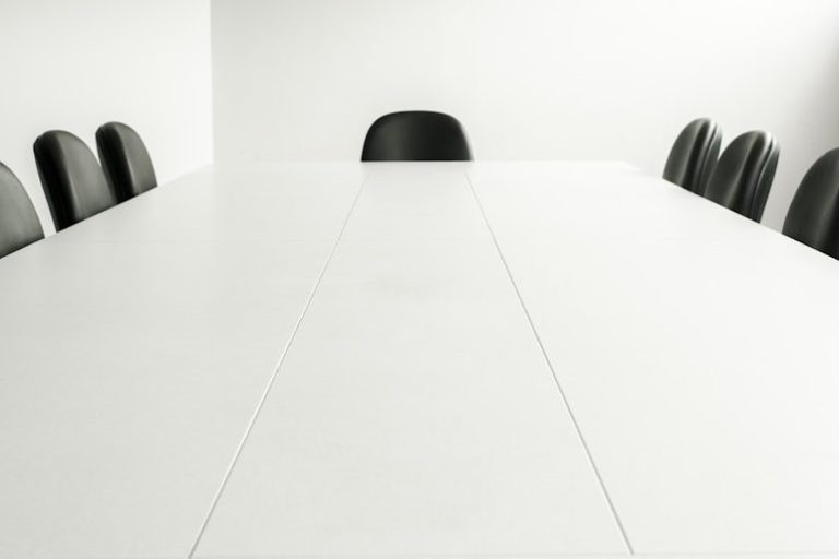 Leerer Konferenztisch mit einem Stuhl am Ende, neutrale Farbgebung.