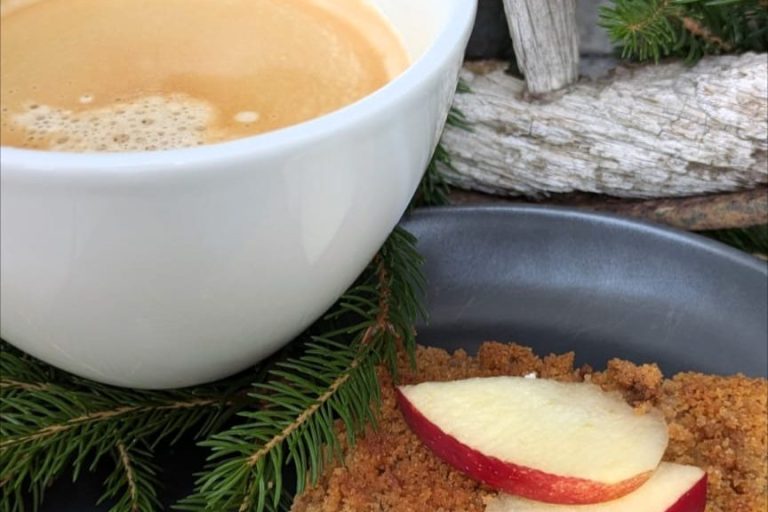 Tasse Kaffee neben einem Teller mit Apfelstücken auf einem rustikalen Tisch.