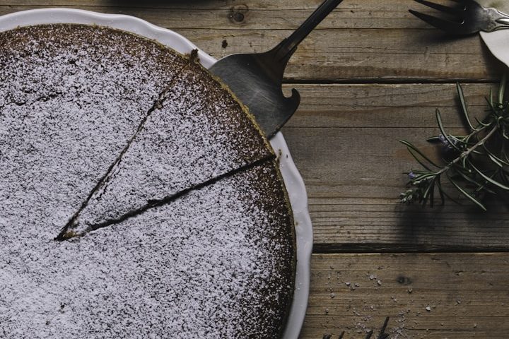 Schokoladenkuchen mit Puderzucker, teilweise in Stücke geschnitten, auf Holzoberfläche.